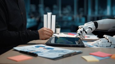 Verimlilik araçları ve belgelerle çevrili bir tablet kullanarak dijital analiz üzerinde çalışan bir insan eli ve robot eli gösteren gelecekçi bir çalışma alanı. Noogenesis