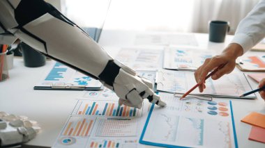 Modern bir ofiste veri analizi üzerinde çalışan bir insan eli ve robot kolu gösteren büyüleyici bir görüntü, takım çalışmasını ve teknoloji entegrasyonunu vurguluyor. Noogenesis