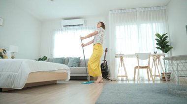 Modern apartman dairesinde dans ederken yerleri paspaslayan beyaz bir hizmetçi. Mutlu enerjik anne ya da temizlikçi müzik eşliğinde oturma odasını temizlemekten zevk alır. Yaşam tarzı. Pedagoji.