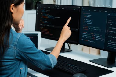 İnternet sitesinde kodlama programı uygulaması olan ve kot gömlek giyen bilgisayar hakkında bilgi veren IT geliştiricisi genç bir Asyalı kız. Güvenlik programlarıyla çevrili iki ekran. Taktik.
