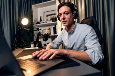 Sunucu kanalı akıllı yayıncı laptopta canlı sosyal medya uygulaması arıyor, kulaklık takıyor ve modern ofis stüdyosundaki mikrofonu kullanıyor. Bireysel.