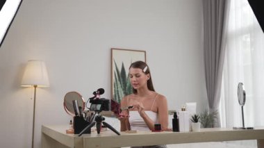 Sosyal medya için güzellik ve kozmetik video içeriği hazırlayan genç bir kadın. Güzellik blogcusu kameraya gülümserken seyircilere ve takipçilere güzellik bakımını gösteriyor. Düzenle