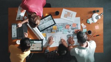 İnşaat mühendisi ekibi toplantıda beklerken yapışkan nota bakıyor. Tasarımcının çalışmasına ve notlara bakmasına ilişkin en üst görünüm, meslektaşı açıklama yaparken ve birlikte çalışırken planda yer alıyor. Sempozyum.