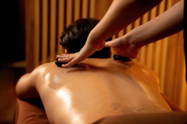 Sıcak mum ışığıyla lüks bir tatil köyündeki kaplıca salonunda sıcak taş masajı, mutlu erkek müşteri bazalt taşı masajının keyfini çıkarırken rahatlatıcı bir sıcaklıkla vücudun üzerinde süzülüyor. Sessiz.