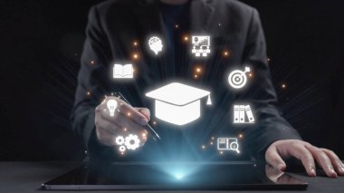 Profesyonel bir adam, modern karanlık bir ortamda bilgi, büyüme ve yeniliği sembolize eden yaratıcı eğitim simgeleriyle çevrili bir tabletle meşgul olur. Dörtgen