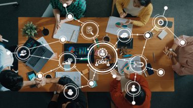 Çeşitli profesyonellerin CRM verilerini ve görselleştirmelerini modern bir çalışma alanında işbirliği ve stratejik planlamayı vurgulayan bir iş toplantısının havadan görüşü. Dostluk