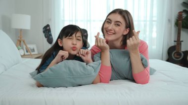 Mutlu Asyalı kız ve akıllı anne kameraya bakarken yatağa uzanıyorlar. Enerjik aile vakit geçirir ve birlikte yatmaya hazırlanır. Sevimli kız ve anne kameraya gülümsüyor sevgi ve şefkat gösteriyorlar. Pedagoji.