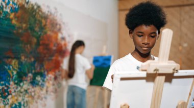 Akıllı Afrikalı çocuk tuvali boyarken, tatlı kız da arkadan çiziyor. Sanat dersinde. Lise öğrencisi renkli duvarların önünde durarak yaratıcılık fikri ile sanat eserleri yaratıyor. Öğretim.