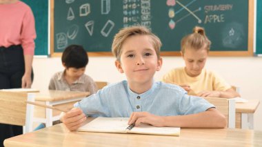 Çekici beyaz çocuk okulda matematik okurken kameraya bakıyor. Çeşitli şirin öğrenciler test yaparken öğretmen Asyalı çocuklara soru sorup tahtaya kağıt doğrultuyor. Pedagoji.