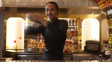 Asyalı akıllı barmen karışık kokteyl sallayarak lüks tezgah hazırlıklarına hazırlanıyor, kameranın önüne bakarak özel bir içecek hazırlıyor. Özel gece hayatı lüksü. Vinosity.
