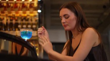 Oturan güzel bir bayan misafir, arkadaşlarıyla beklemekten sıkılıyor ya da Bokeh gece kulübünde lüks bir tezgah barda mavi Hawaii kokteylinde karışık votka içmekten sıkılıyor. Vinosity.