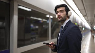 Proje yöneticisi tren istasyonunda şarkı seçmek için cep telefonu tutarken kulaklık takıyor. Zeki iş adamı bulanık geçmişi olan treni beklerken saati kontrol ediyor. Sevinçli..