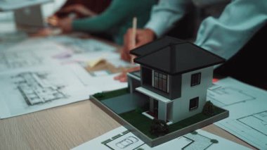 Tasarımcılar işbirliği içindeyken mimari bir model planların ortasında bir masada oturuyor. Görüntü, modern tasarım kavramlarını ve inşaat projelerinde takım çalışmasını yakalıyor. SACTR