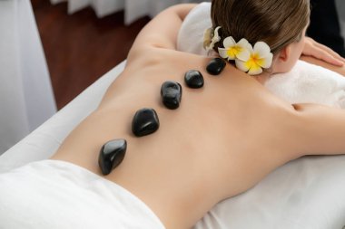 Lüks tatil köyündeki kaplıcalarda sıcak taş masajı. Gün ışığı sükunet ortamında, mutlu kadın müşteri bazalt taş masajından zevk alıyor. Rahatlatıcı bir sıcaklıkla vücudun üzerinde süzülüyor. Sessiz.