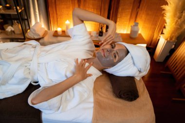 Kaplıca salonunun sakin atmosferi, üst düzey kadın müşteri sıcak mum ışığında kömür kömürü yüz kremi masajıyla kendini yenilemeye çalışıyor. Yüz bakımı ve güzellik konsepti. Sessiz.