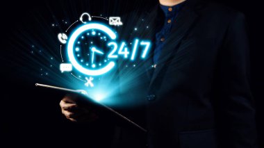 İş adamı, elinde 24 saatlik parlak bir hizmet ikonu bulunan bir tablet tutuyor. Teknoloji odaklı bir ortamda sürekli bulunabilirliği ve modern iletişimi sembolize ediyor. Dörtgen