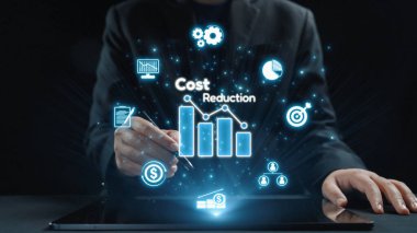 Bir profesyonel, interaktif dijital grafikler ve simgelerle maliyet azaltma stratejilerini analiz etmek ve lüks bir ofis ortamında modern iş çözümleri sergilemek için bir tablet kullanıyor. Dörtgen