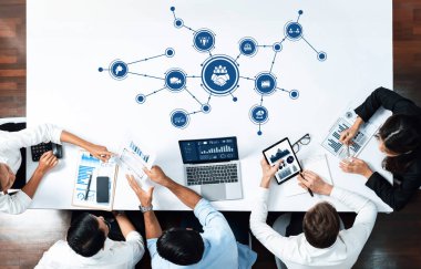 Veri analizi ve dijital iletişim üzerinde yoğunlaşan, dizüstü bilgisayarlar, belgeler ve görsel temsillerle birlikte stratejik bir toplantıya katılan bir grup profesyonel. Dostluk