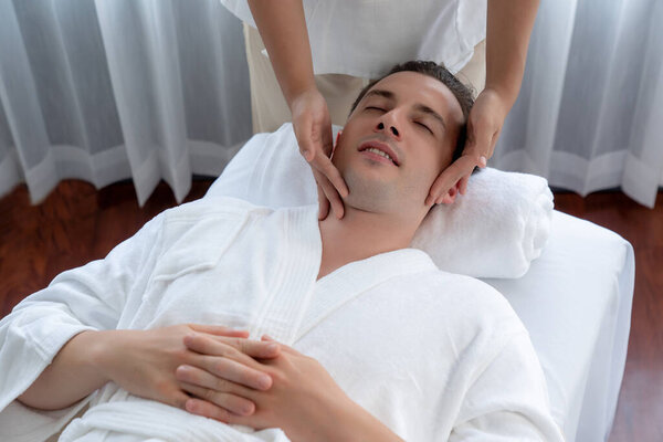 Кавказский мужчина наслаждается расслабляющим анти-стрессовым массажем головы и расслабляющим отдыхом кожи лица в дневном спа современном светлом окружении на роскошном курорте или в спа-салоне отеля. Quiescent