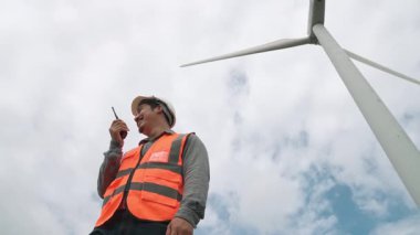Gökyüzü arka planına sahip bir rüzgar türbini üzerinde çalışan mühendis. Yenilenebilir ve sürdürülebilir enerjinin gelecekteki üretimi için yenilikçi bir ideal. Rüzgar türbininden enerji üretimi.