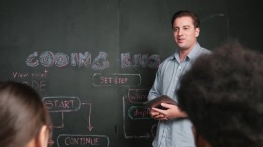 Tableti gemide tutarken akıllı öğretmen kodlama sistemini öğretiyor. BTMM teknoloji sınıfında dizüstü bilgisayar yazma programı kullanarak çalışan melez ırklı çekici bir genç. Yenilikçi. Öğretim