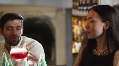 Süslü çam neon karlı bir gece kulübünde süslü püslü çam ağacından konuşan ve kokteyl içen gülümseyen bir kadın. Vinosity.