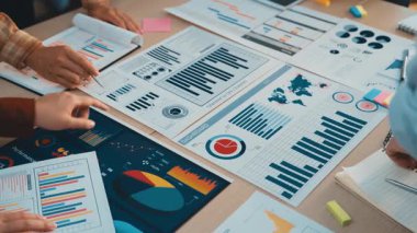 İş ortamında işbirliği ve stratejik planlamayı simgeleyen renkli çizelgeler ve grafiklerle el ele tutuşan çekici bir sahne. SACTR