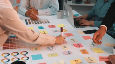 Değişik bir ekibin ortaklaşa bir projeye katıldığı canlı bir ofis sahnesi. Renk örnekleri, yapışkan notlar ve dizüstü bilgisayarlar yaratıcılık ve takım çalışmasının atmosferini gösteriyor. SACTR