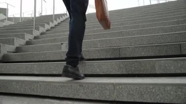 Akıllı bir iş adamının elinde çantayla merdivenlerden yukarı çıkışının en üst görüntüsü. Profesyonel proje yöneticisi merdivenlerden çıkıp işyerine gidiyor. Yeteneklerini arttırmak, terfi almak, seyahat etmek. Sevinçli..