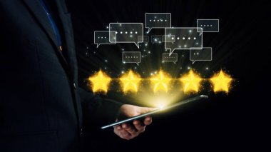Bir işadamı, beş parlayan yıldız ve sohbet baloncuğu ikonlarıyla çevrili bir tablet kullanarak müşteri geribildirimi ve dijital iletişimin önemini gösteriyor. Dörtgen