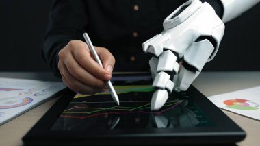 Robot bir elin tabletle etkileşimini gösteren dinamik bir sahne, çağdaş ofis düzeninde grafikler ve grafikler yoluyla veri analizlerini gösteriyor. Noogenesis