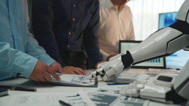 Veri analizi ve raporlama hazırlıklarında takım çalışmalarını vurgulayan, modern bir ofiste iş dünyasından profesyonellerle işbirliği yapan robotik bir eli gösteren fütüristik bir sahne. Noogenesis