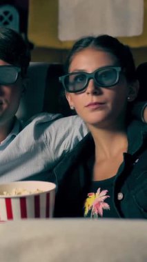 Sinemada üç boyutlu gözlüklü bir kadın ve erkek film izliyor. Ekrana bakar, heyecan verici ve patlamış mısır yer.