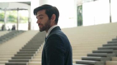 Akıllı iş adamı merdivenlerde kameraya bakıyor. İş elbisesi giyerken kameraya gülümseyen başarılı adamın yakın çekimi. Yönetici, kameraya bak. Hareket eden kamera. Sevinçli..