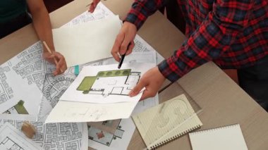 Mimari döküman, ölçüm araçları ve ahşap blokların modern ofiste etrafa saçıldığı masa üzerine planlar yapma konusunda akıllı mimar ve güvenlik mühendisi tartışması. - Yakın çekim. Tanımlama.