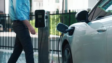 İlerici işadamı, şehir merkezinde dolaşmadan önce şarj cihazından elektrikli arabasına şarj prizi takıyor. Çevre dostu şarj edilebilir araba, sürdürülebilir ve temiz enerjiyle çalışıyor..