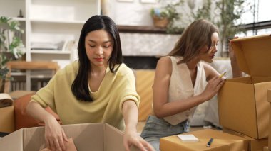 Çekici bir oda arkadaşı oturma odasında paket paketlerken pakette konum yazıyor. Mutlu satıcı birlikte çalışıyor ve teslimat paketini hazırlıyor. Girişimci kargo kutusu paketliyor. Myrmidon.