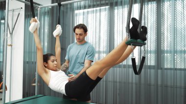 Pilates eğitmeni, Cadillac teçhizatı üzerinde asılı duran bir bacak egzersizinde bir müşteriye rehberlik ediyor. Vücut dengesini sağlamak için Cadillac 'ı geren sağlıklı bir kadın. Alışkanlık.