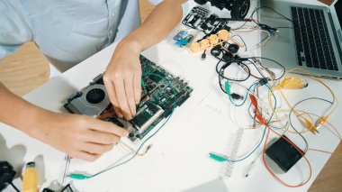 Masadaki elektronik aletle ana kartı tamir eden çocuğa yakın çekim. Elektronik teçhizatla lise öğrencilerinin elektrik panosunun en üst görüntüsü, kablo aletleri masanın etrafına saçılmış. Öğretim.