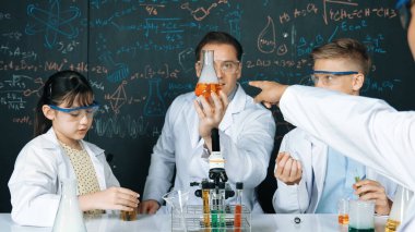 Akıllı öğretmen deney kabında çözeltiyi tutarken öğrenci BTMM fen dersinde kimya teorisiyle karatahta deney yapıyor. Kimyasal sıvıyı laboratuvarda inceleyen yetenekli bir bilim adamı. Öğretim.