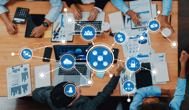 Bir grup profesyonel iş toplantısı sırasında işbirliği yapıyor, verileri analiz ediyor ve ahşap bir masa üzerinde teknoloji ve görsel grafikler kullanarak fikir alışverişinde bulunuyor. Dostluk