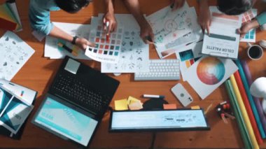 Tasarımcı fikirleri yazarken proje yöneticisinin yukarıdan aşağıya bakan görüntüsü. Akıllı iş adamları logo tasarımı fikrini açıklarken tasarımcılar palete bakarken temayı seçiyorlar. Sempozyum.