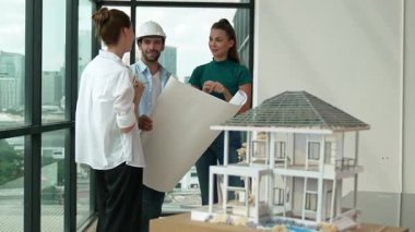 Profesyonel mimar mühendis ekibi konuşuyor, paylaşıyor, tasarım hakkında beyin fırtınası yapıyor. Yönetici planı dinlerken genç mimar plan yapıyor. İzleme