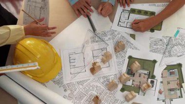 Mimari belge, ölçüm aracı ve ahşap blokların modern ofiste etrafa saçıldığı bir masa üzerinde yapı inşaatı ile ilgili mimar ve güvenlik mühendisi tartışması. Tanımlama.