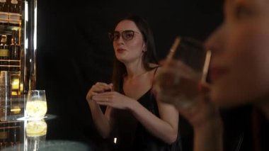 Parlak gece partisinde lüks bir gece kulübünde özel içkide gözlüklü güzel bir kadının portresi. Barda oturmuş, barmen ve arkadaşlarıyla atmosfer partisi saatleri hakkında konuşuyor. Vinosity.