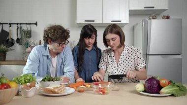 Çekici beyaz anne ve baba Asyalı kızıyla taze yemek pişirmek için birlikte vakit geçiriyorlar. Enerjik anne ve baba mutfakta salata yapmak için taze sebze hazırlıyor. Sağlıklı yiyecekler. Pedagoji.