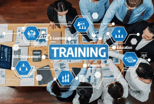 Ahşap bir masa üzerindeki tablolar, veriler ve dijital öğrenme araçlarıyla çevrili, ilgi çekici bir eğitim oturumuna katılan çeşitli profesyonellerin hava görüşü. Dostluk