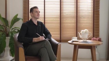 Psikiyatri ofisinde ya da terapi odasında koltukta oturan erkek psikolog. Arkadaş canlısı ve profesyonel ruh sağlığı danışmanı ve terapisti. Düzenle