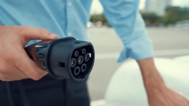 İlerici işadamı, şehir merkezinde dolaşmadan önce şarj cihazından elektrikli arabasına şarj prizi takıyor. Çevre dostu şarj edilebilir araba, sürdürülebilir ve temiz enerjiyle çalışıyor..