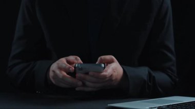 Akıllı telefon tutan bir kişi, büyümeye yönelik finansal stratejileri sembolize ederek, karanlık bir arkaplanda maliyet azaltma ve iş analizlerini temsil eden sanal simgeler sergiliyor. Dörtgen